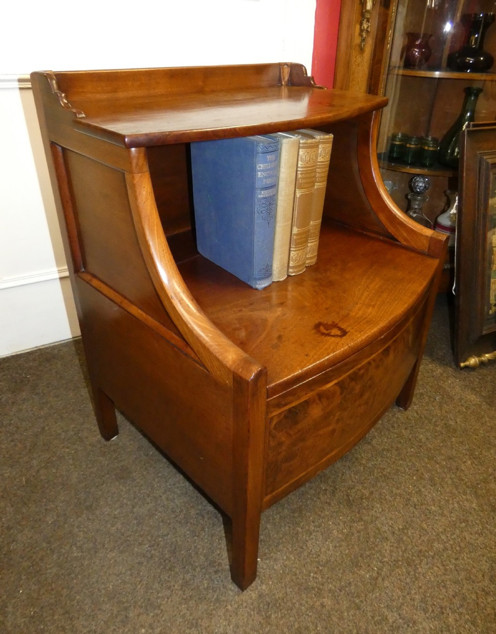 An antique Georgian mahogany bedside commode featuring an open upper shelf section with curved sides and a veneered lower cabinet.