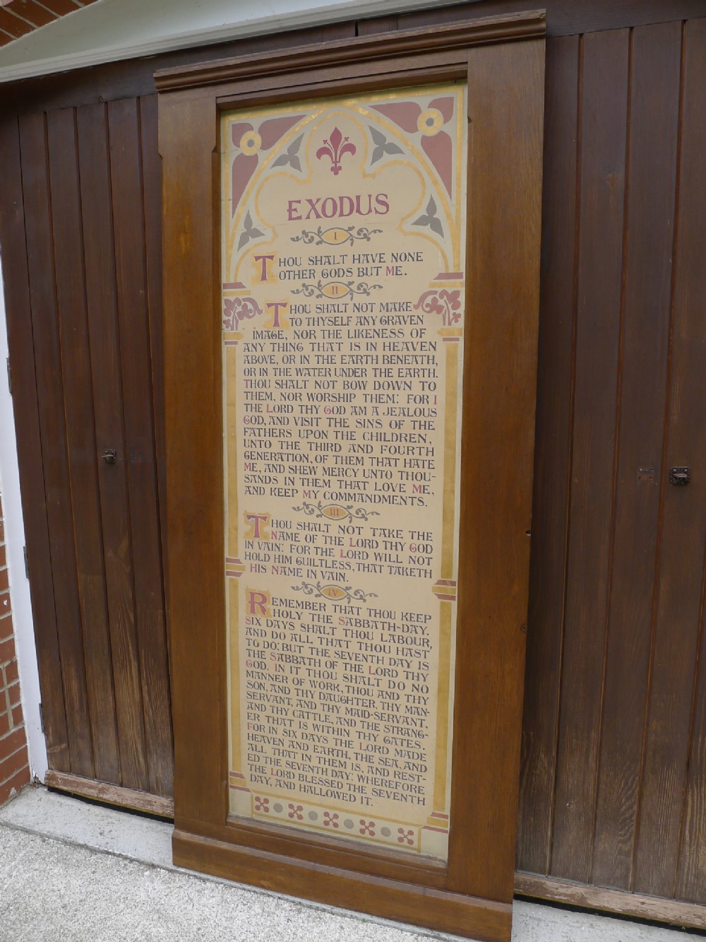 A tall Victorian oak framed wall panel featuring hand-painted illuminated biblical text from Exodus inside a decorated arch.