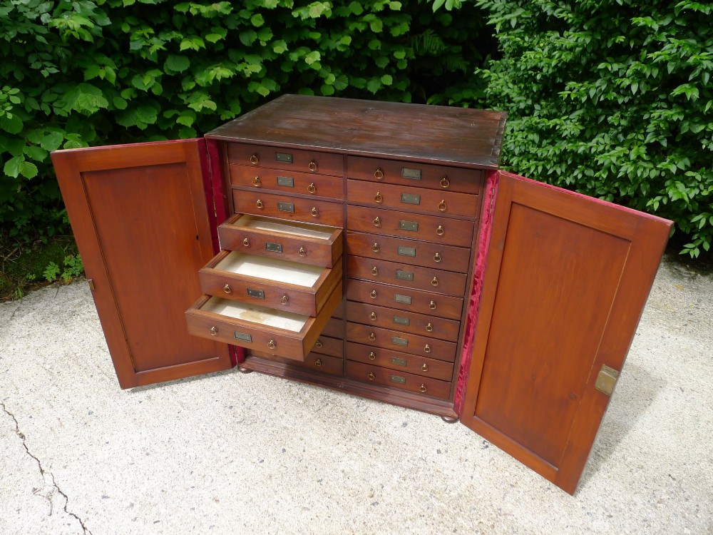 A mid-19th-century stained deal collectors cabinet featuring double doors opened to reveal twenty drawers with brass handles. View IX