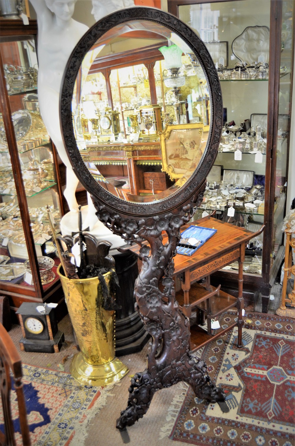 A 19th-century Chinese freestanding mirror featuring a circular glass face enclosed in a dark cherrywood frame carved with naturalistic prunus blossom branches.