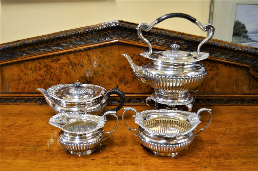 A complete four-piece Victorian silver tea set featuring fluted bodies, scrolling handles, and ornate rims displayed on a wooden surface.