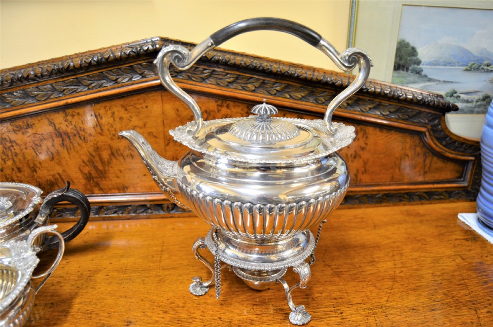 A complete four-piece Victorian silver tea set featuring fluted bodies, scrolling handles, and ornate rims displayed on a wooden surface. View II