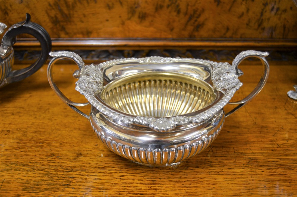 A complete four-piece Victorian silver tea set featuring fluted bodies, scrolling handles, and ornate rims displayed on a wooden surface. View III