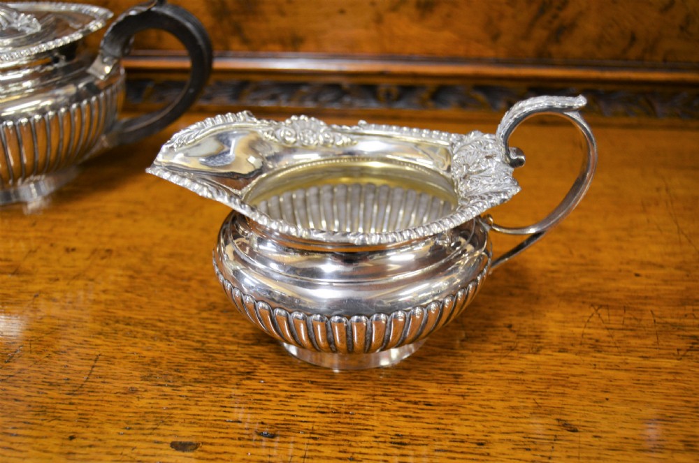 A complete four-piece Victorian silver tea set featuring fluted bodies, scrolling handles, and ornate rims displayed on a wooden surface. View IV