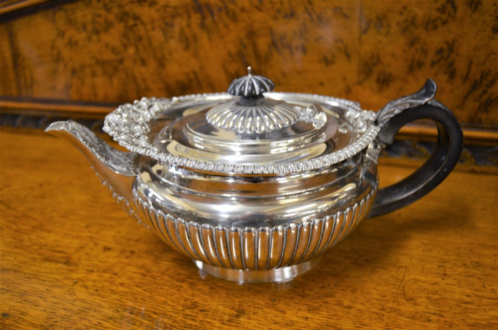 A complete four-piece Victorian silver tea set featuring fluted bodies, scrolling handles, and ornate rims displayed on a wooden surface. View V