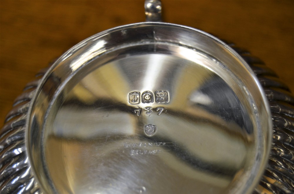 A complete four-piece Victorian silver tea set featuring fluted bodies, scrolling handles, and ornate rims displayed on a wooden surface. View VI