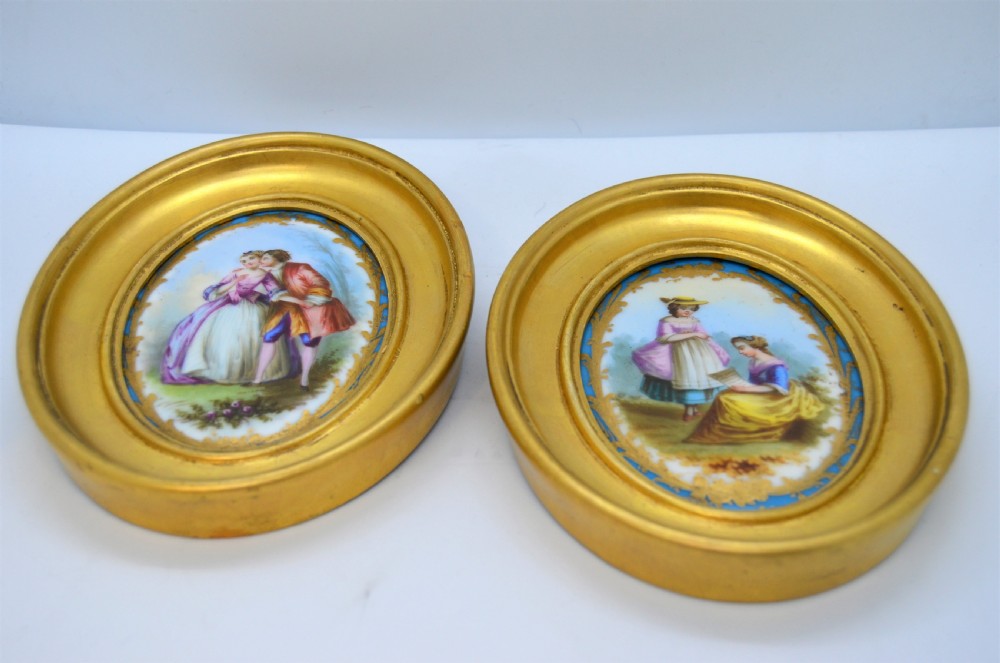A pair of oval gilt-framed porcelain plaques featuring hand-painted pastoral figures within sky blue and gold scroll borders. View II
