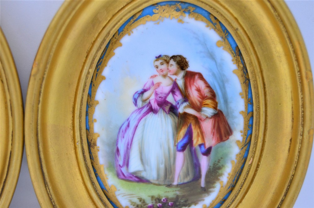 A pair of oval gilt-framed porcelain plaques featuring hand-painted pastoral figures within sky blue and gold scroll borders. View IV