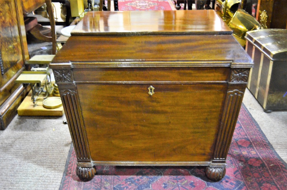 A Regency mahogany wine cooler featuring a sarcophagus shape, fluted corner pilasters, carved rosettes, a brass keyhole escutcheon, and gadrooned feet.
