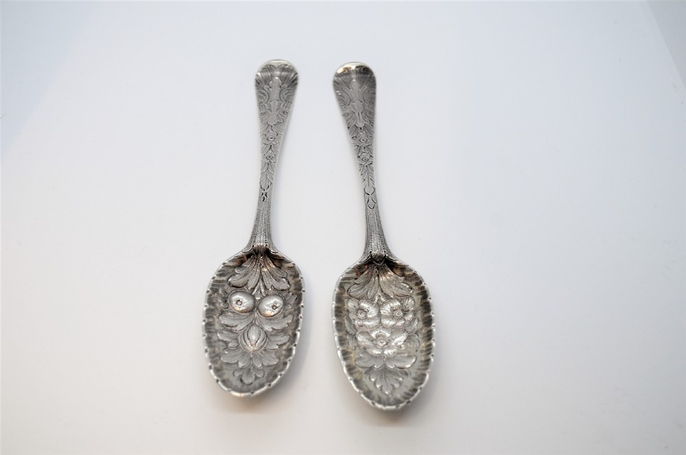 A pair of 18th-century Irish sterling silver spoons featuring embossed fruit and leaf designs in the bowls and chased pattern handles.