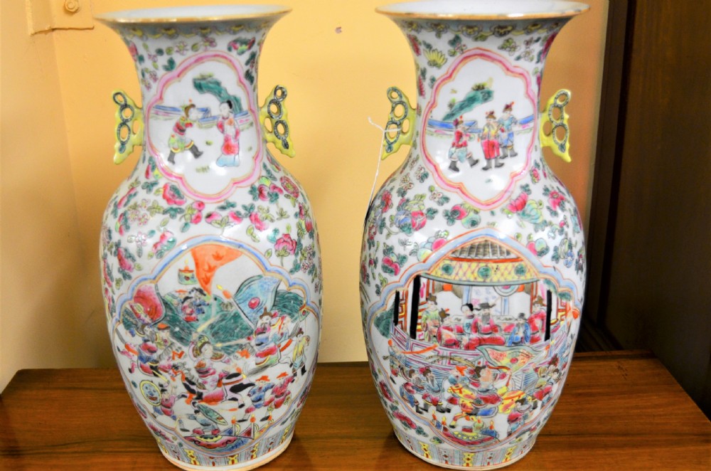 A pair of 19th-century Chinese Famille Rose porcelain baluster vases decorated with hand-painted narrative scenes inside cartouches and yellow pierced handles.