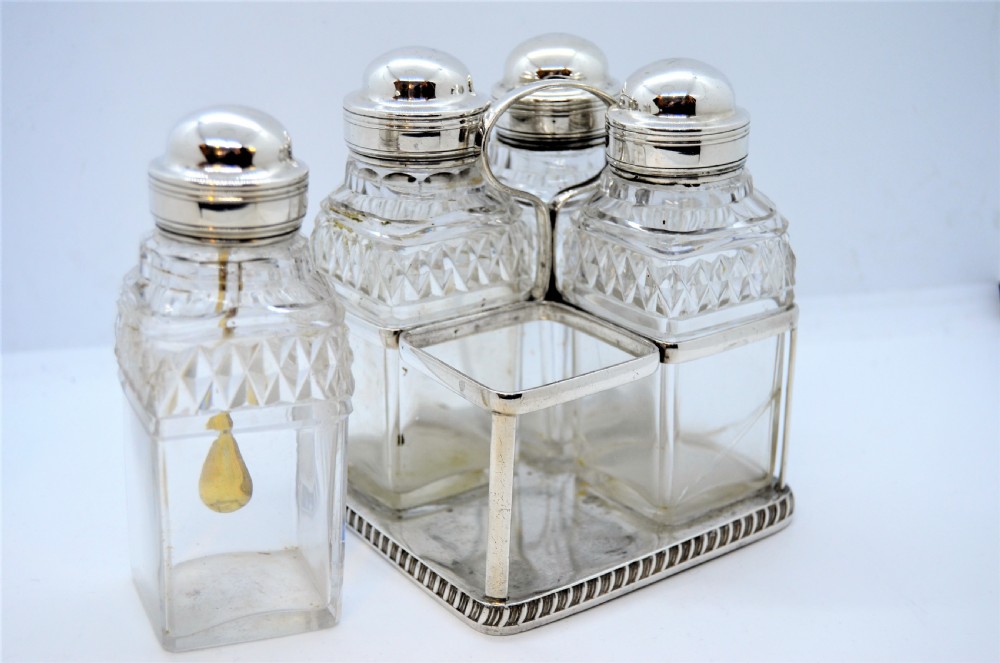 A Georgian silver cruet frame holding four square cut glass condiment bottles with silver domed caps and a central loop handle.