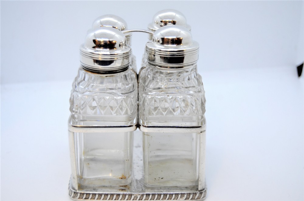 A Georgian silver cruet frame holding four square cut glass condiment bottles with silver domed caps and a central loop handle. View II