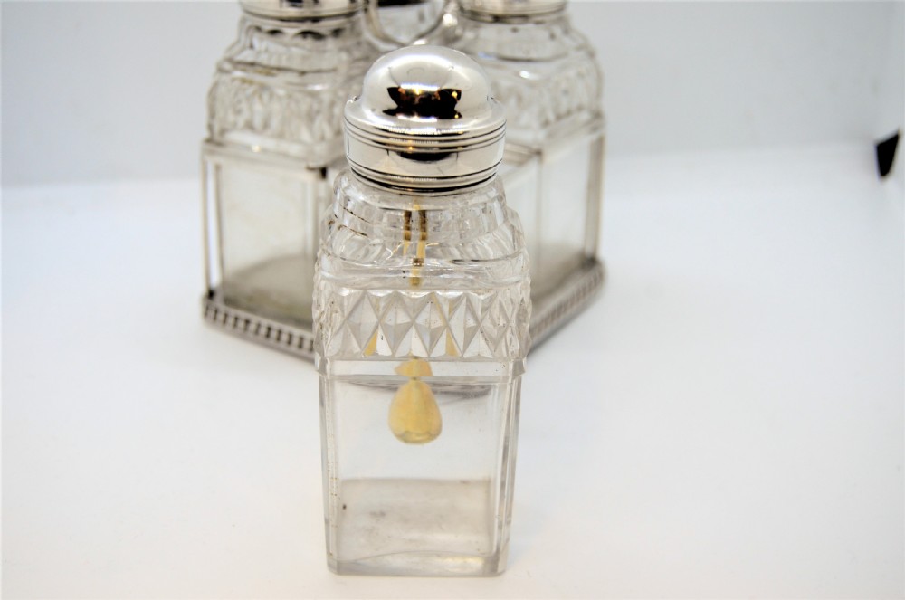 A Georgian silver cruet frame holding four square cut glass condiment bottles with silver domed caps and a central loop handle. View III