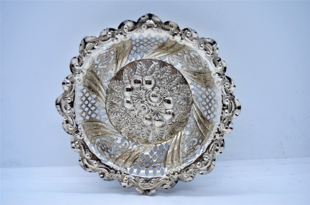 A round Victorian silver dish featuring a pierced lattice pattern, scalloped rim, and embossed floral center motif.