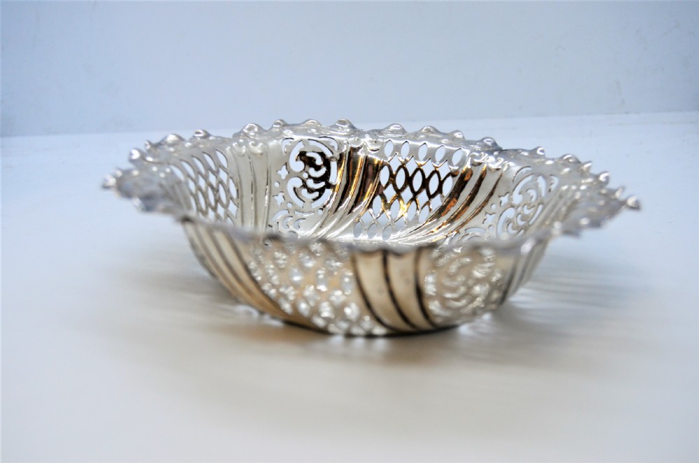 A round Victorian silver dish featuring a pierced lattice pattern, scalloped rim, and embossed floral center motif. View IV