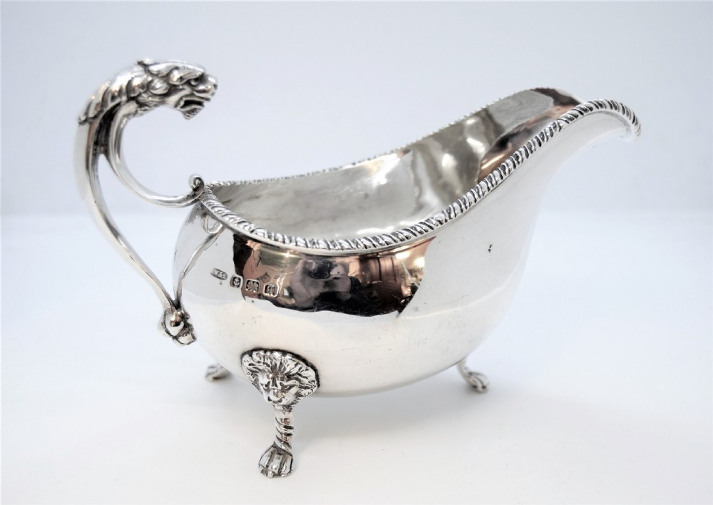 A polished sterling silver sauce boat featuring a serpent head handle, gadrooned rim, and three lion mask feet with visible hallmarks.