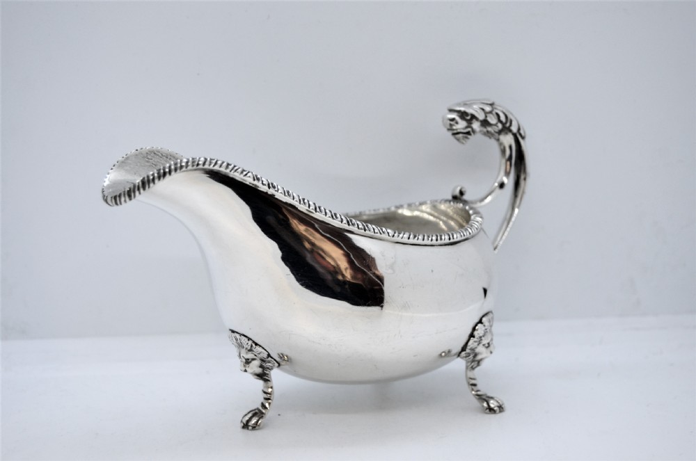 A polished sterling silver sauce boat featuring a serpent head handle, gadrooned rim, and three lion mask feet with visible hallmarks. View IV