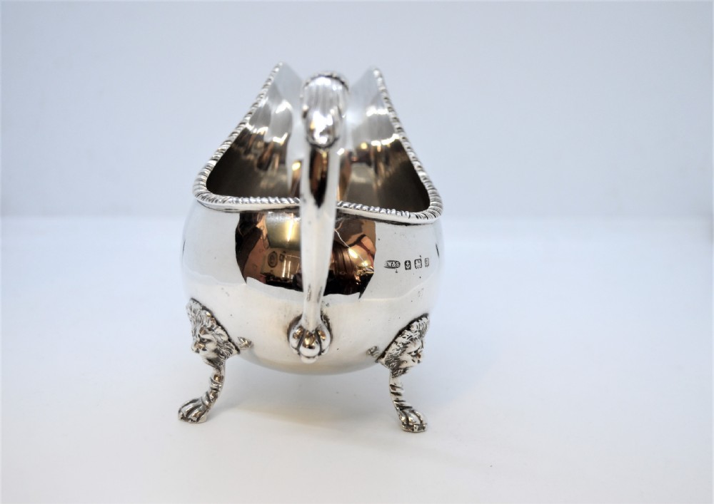 A polished sterling silver sauce boat featuring a serpent head handle, gadrooned rim, and three lion mask feet with visible hallmarks. View VII