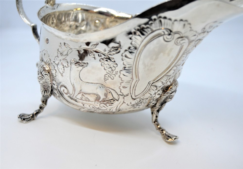 An antique Irish sterling silver cream jug featuring detailed repousse chasing of animals, lion-headed tripod legs, and a scroll handle. View III