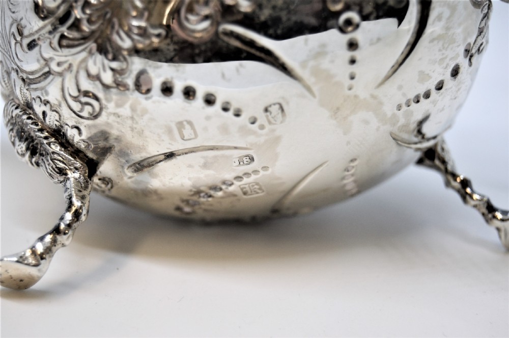 An antique Irish sterling silver cream jug featuring detailed repousse chasing of animals, lion-headed tripod legs, and a scroll handle. View IV