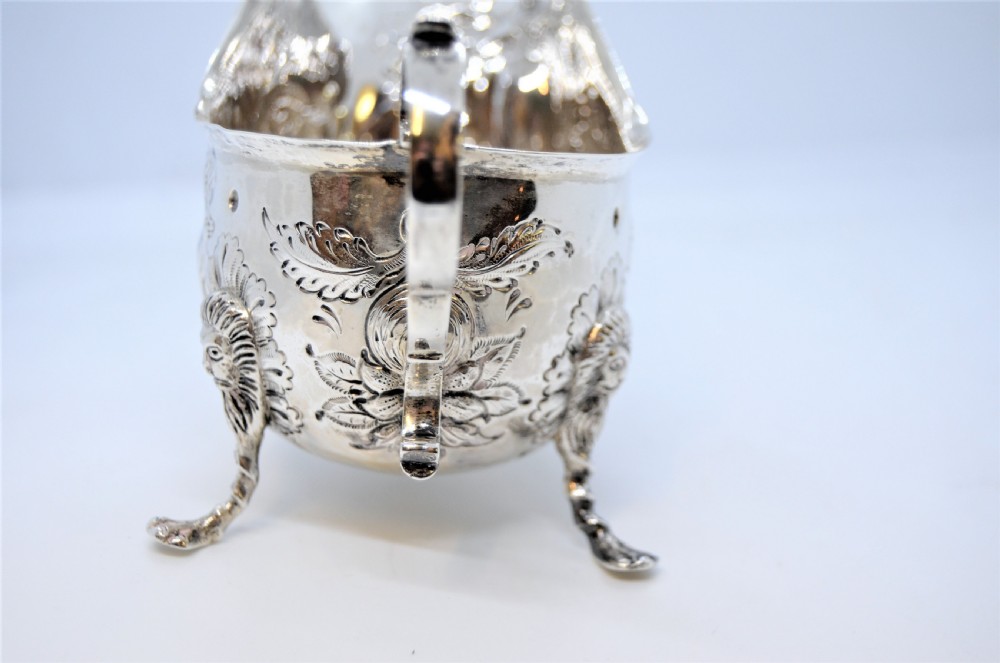 An antique Irish sterling silver cream jug featuring detailed repousse chasing of animals, lion-headed tripod legs, and a scroll handle. View V