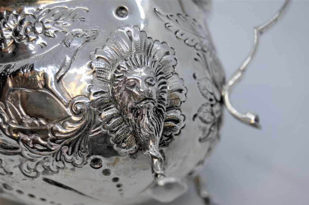 An antique Irish sterling silver cream jug featuring detailed repousse chasing of animals, lion-headed tripod legs, and a scroll handle. View VI