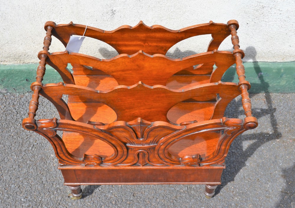 A Victorian mahogany canterbury featuring three carved slotted compartments, a lower drawer with a turned knob, and turned legs with brass castors. View II