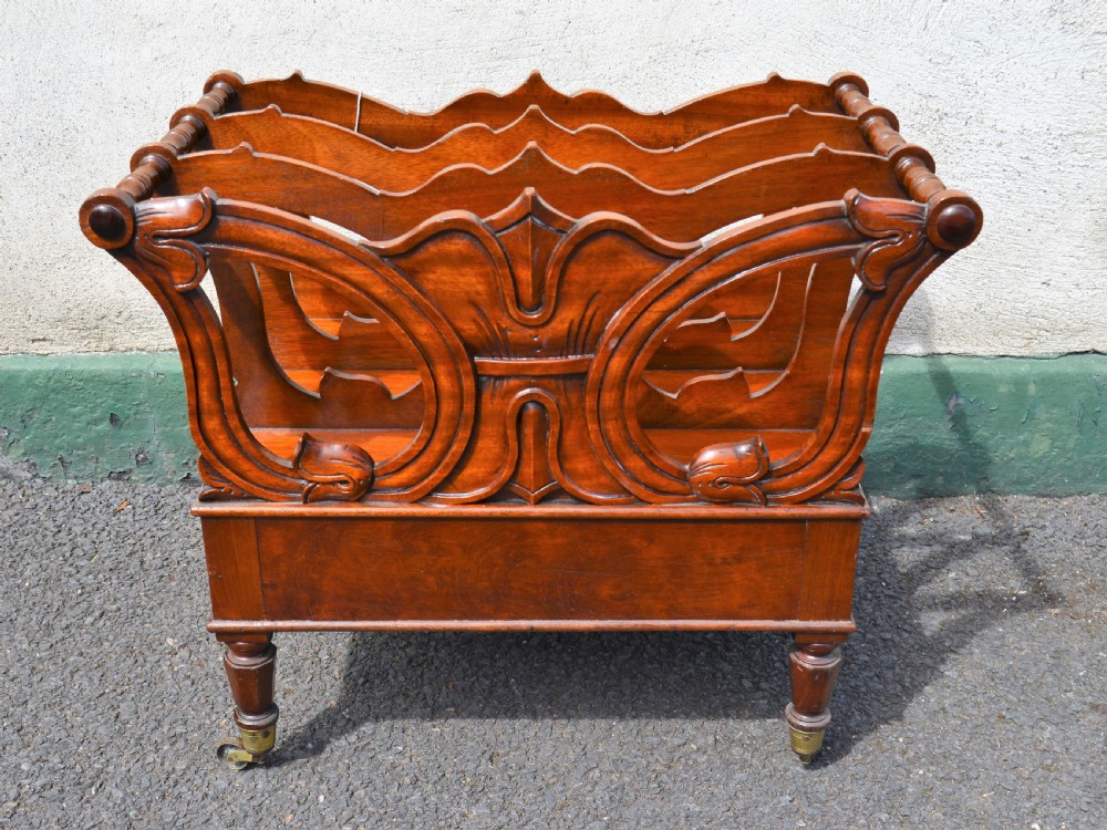 A Victorian mahogany canterbury featuring three carved slotted compartments, a lower drawer with a turned knob, and turned legs with brass castors. View IV