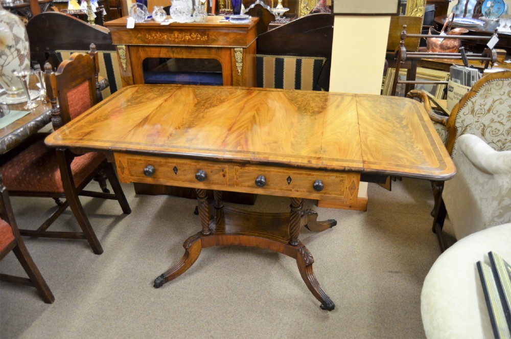 A Regency flame mahogany sofa table featuring two drop-leaf sides, two front drawers with turned wooden knobs, twin spiral-turned pedestal columns, and splayed legs ending in brass castors. View III