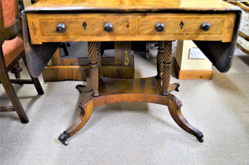 A Regency flame mahogany sofa table featuring two drop-leaf sides, two front drawers with turned wooden knobs, twin spiral-turned pedestal columns, and splayed legs ending in brass castors. View IV