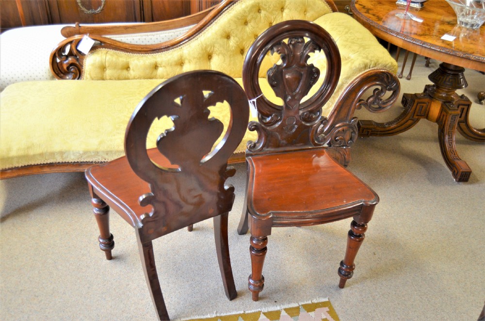 Pair of antique Victorian mahogany hall chairs featuring open carved circular shield backrests, solid timber seats, and turned front legs. View II