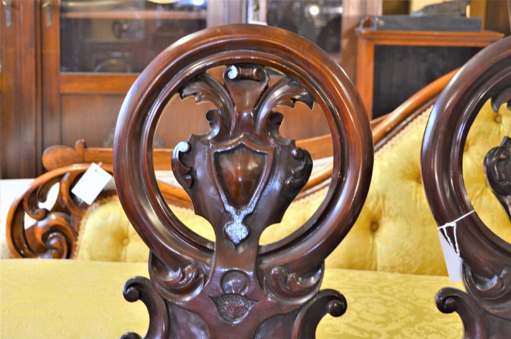 Pair of antique Victorian mahogany hall chairs featuring open carved circular shield backrests, solid timber seats, and turned front legs. View III
