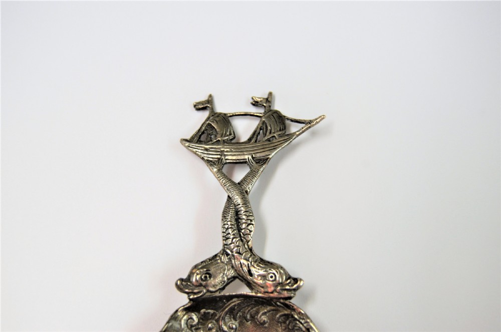 A Dutch silver caddy spoon featuring an embossed figural scene inside the scalloped bowl and a handle formed of entwined sea creatures topped with a sailing ship finial. View III