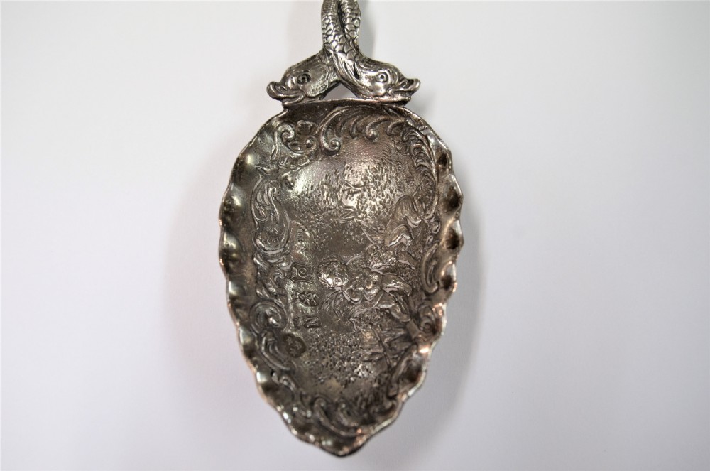 A Dutch silver caddy spoon featuring an embossed figural scene inside the scalloped bowl and a handle formed of entwined sea creatures topped with a sailing ship finial. View IV