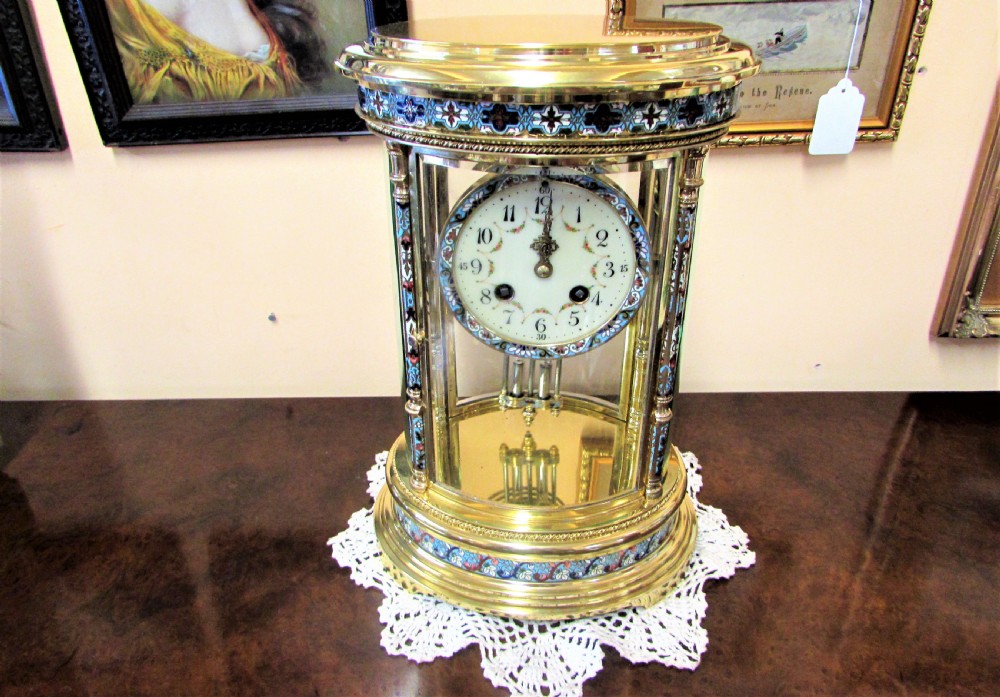 An oval Victorian brass four glass mantel clock featuring colourful cloisonne enamel floral borders and a porcelain dial.