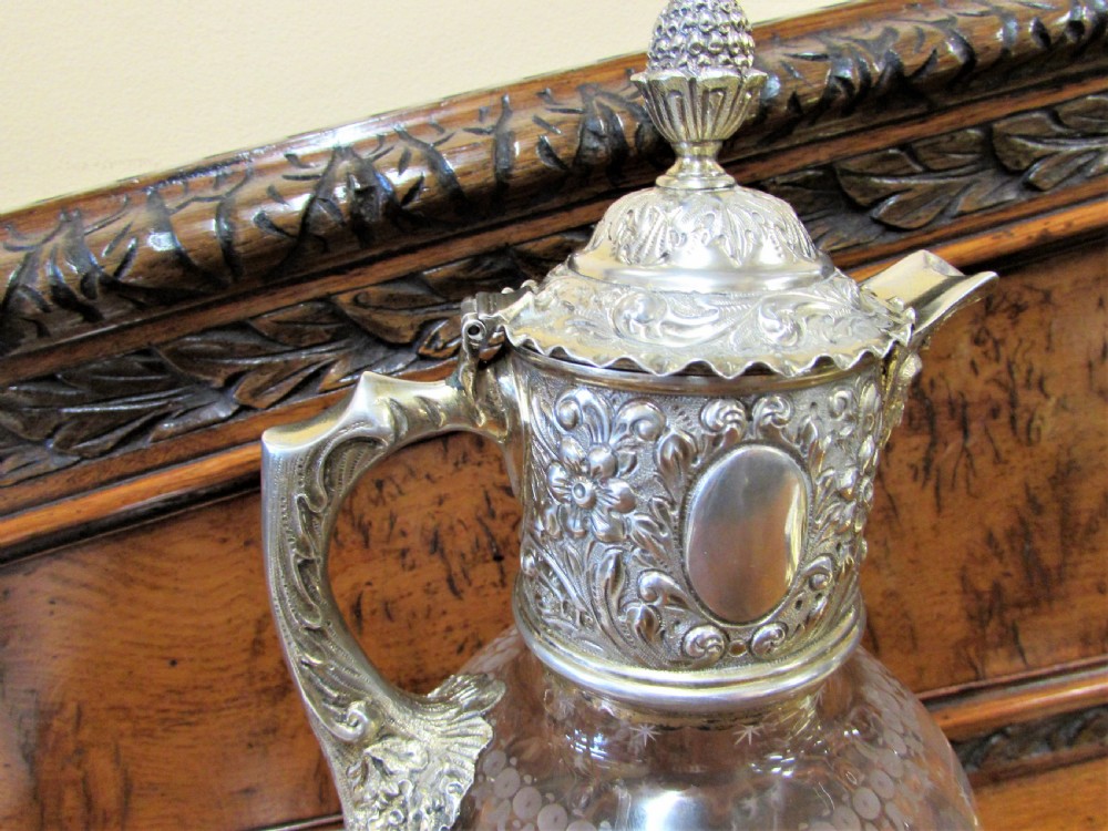 An antique clear glass claret jug decorated with etched star motifs and featuring a silver-plated repousse collar, handle, and finial lid. View II