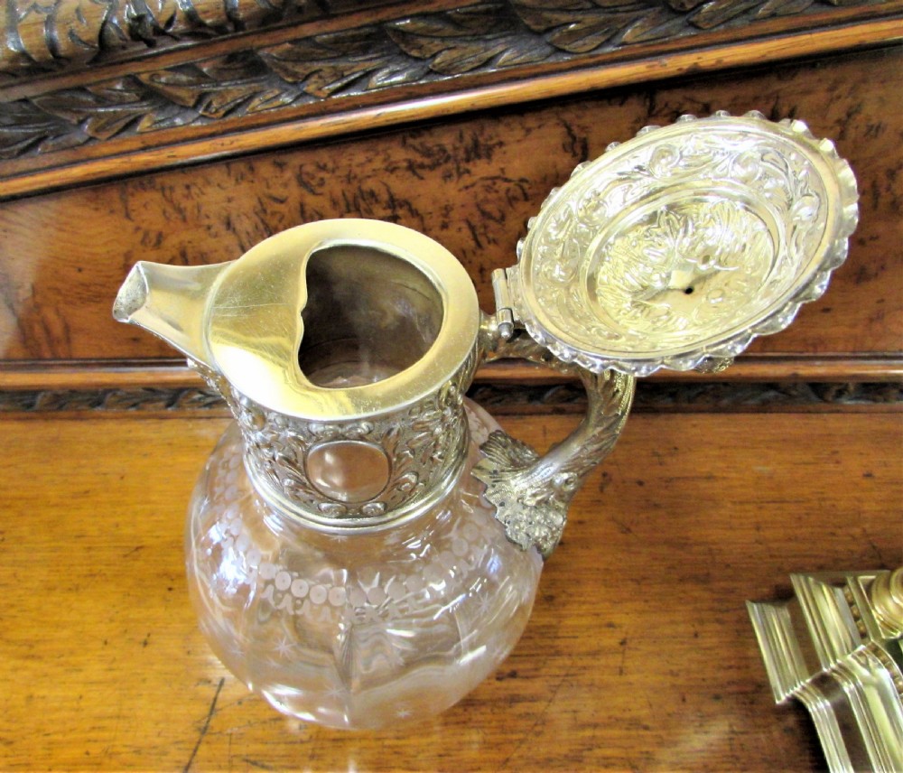 An antique clear glass claret jug decorated with etched star motifs and featuring a silver-plated repousse collar, handle, and finial lid. View III