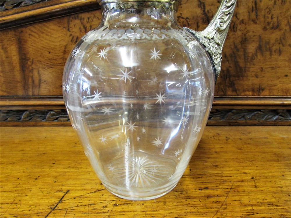 An antique clear glass claret jug decorated with etched star motifs and featuring a silver-plated repousse collar, handle, and finial lid. View IV
