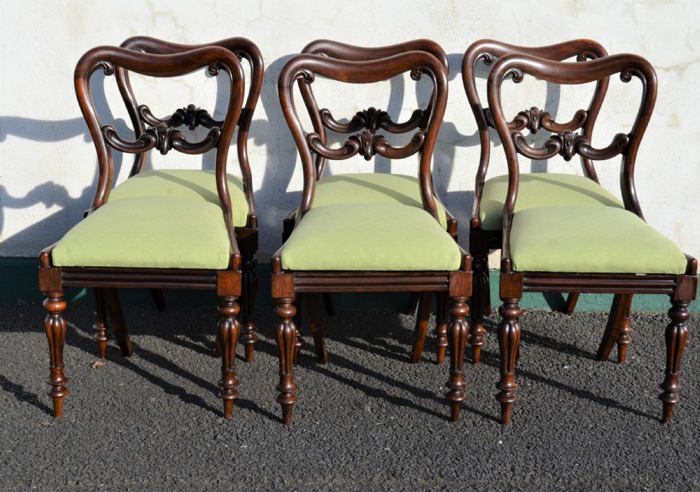 A set of six Victorian rosewood balloon-back dining chairs featuring carved cross-rails, turned front legs, and light green upholstered seats.