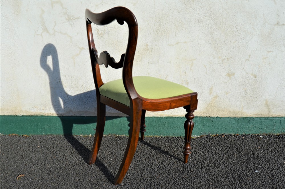 A set of six Victorian rosewood balloon-back dining chairs featuring carved cross-rails, turned front legs, and light green upholstered seats. View V