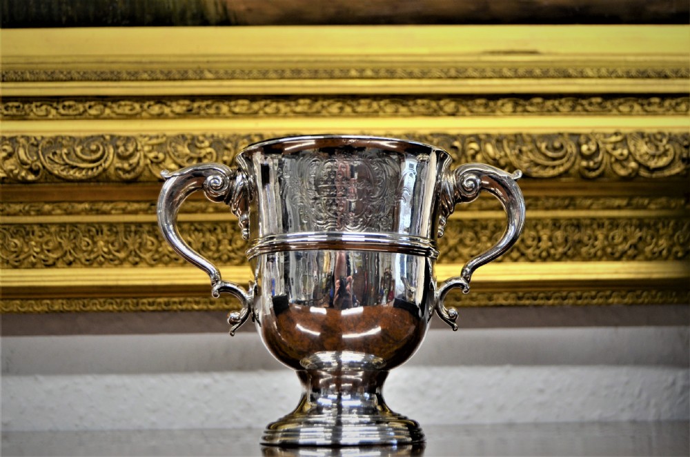 An 18th-century silver two-handled cup featuring an engraved crest, double-scroll handles, a central moulding, and a circular pedestal foot.