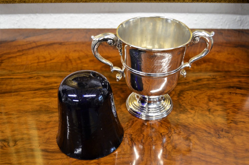 An 18th-century silver two-handled cup featuring an engraved crest, double-scroll handles, a central moulding, and a circular pedestal foot. View IV