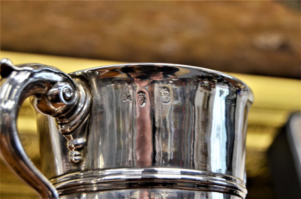 An 18th-century silver two-handled cup featuring an engraved crest, double-scroll handles, a central moulding, and a circular pedestal foot. View V