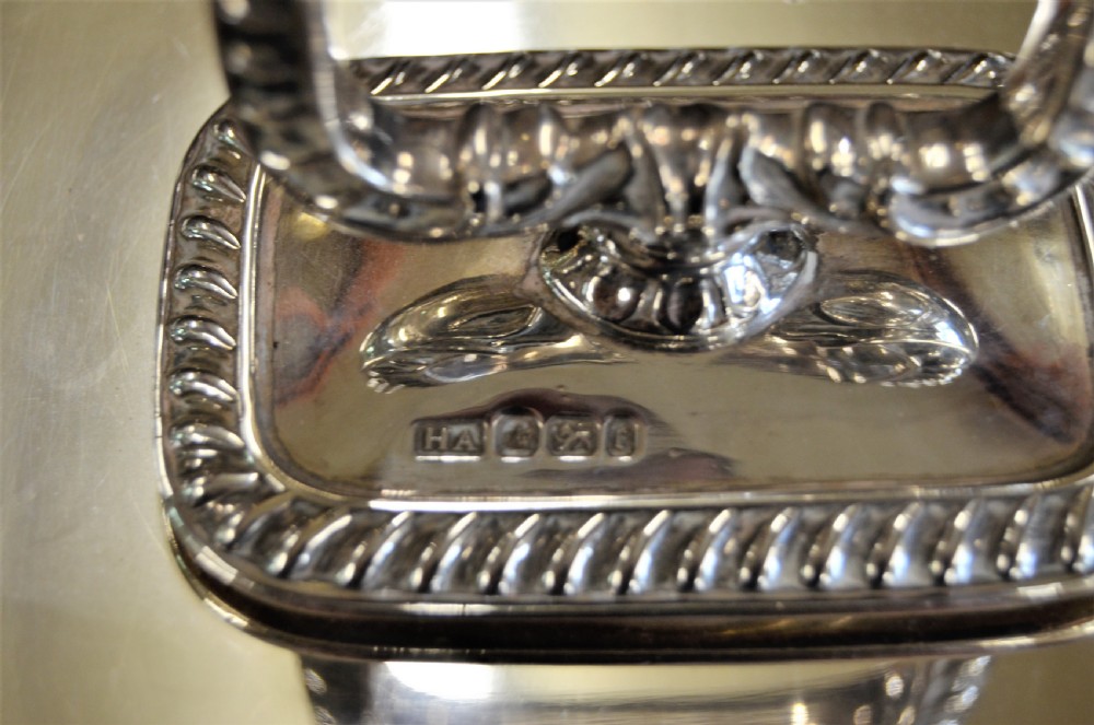 An angled close-up view of an antique rectangular silver entree dish with a matching lid and a loop handle resting on a dark wooden surface. View VI