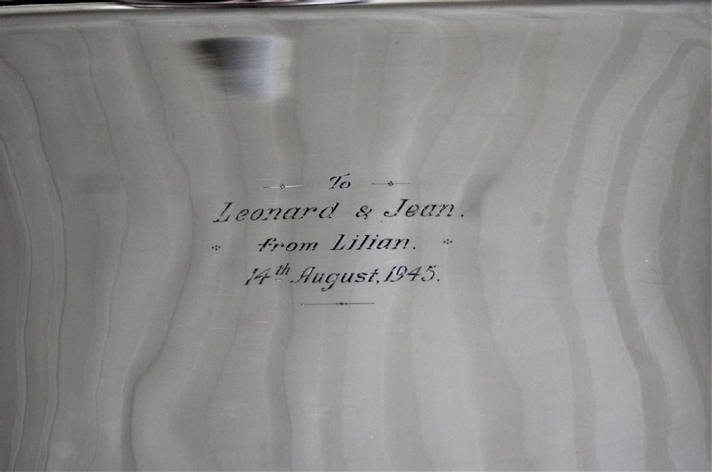 An angled close-up view of an antique rectangular silver entree dish with a matching lid and a loop handle resting on a dark wooden surface. View VII