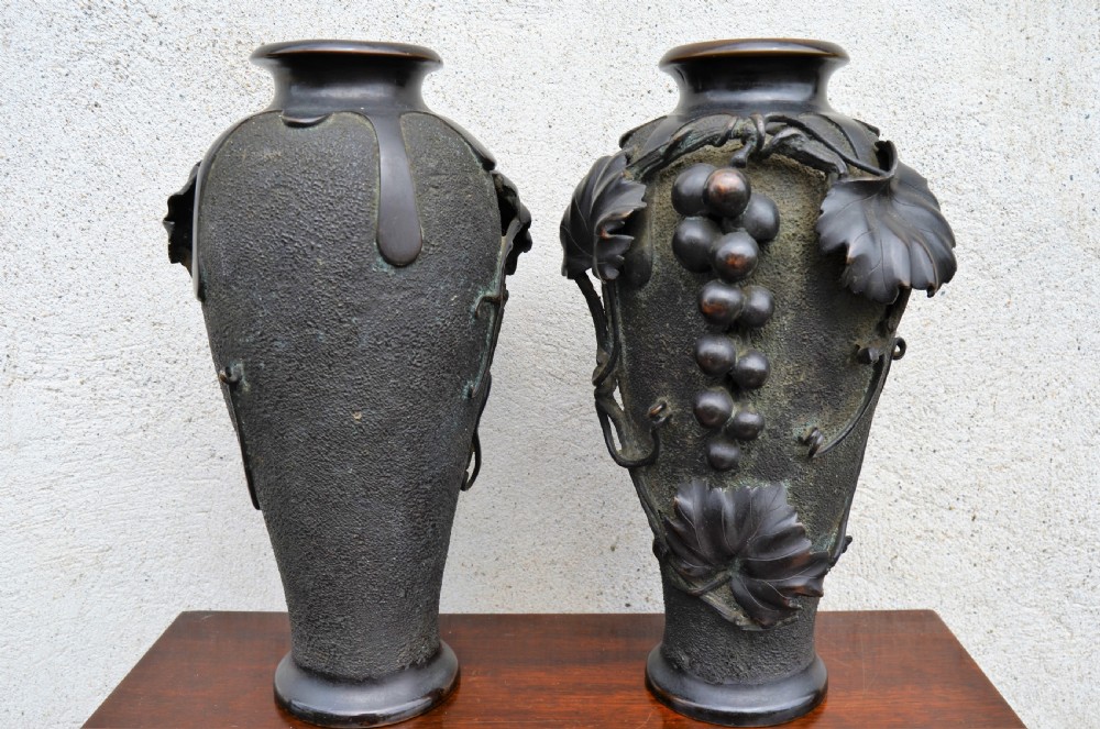 A pair of dark patinated bronze vases decorated with high-relief carved grapevine motifs and fruit clusters over a textured surface. View II