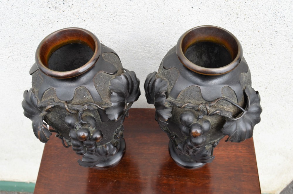 A pair of dark patinated bronze vases decorated with high-relief carved grapevine motifs and fruit clusters over a textured surface. View IV