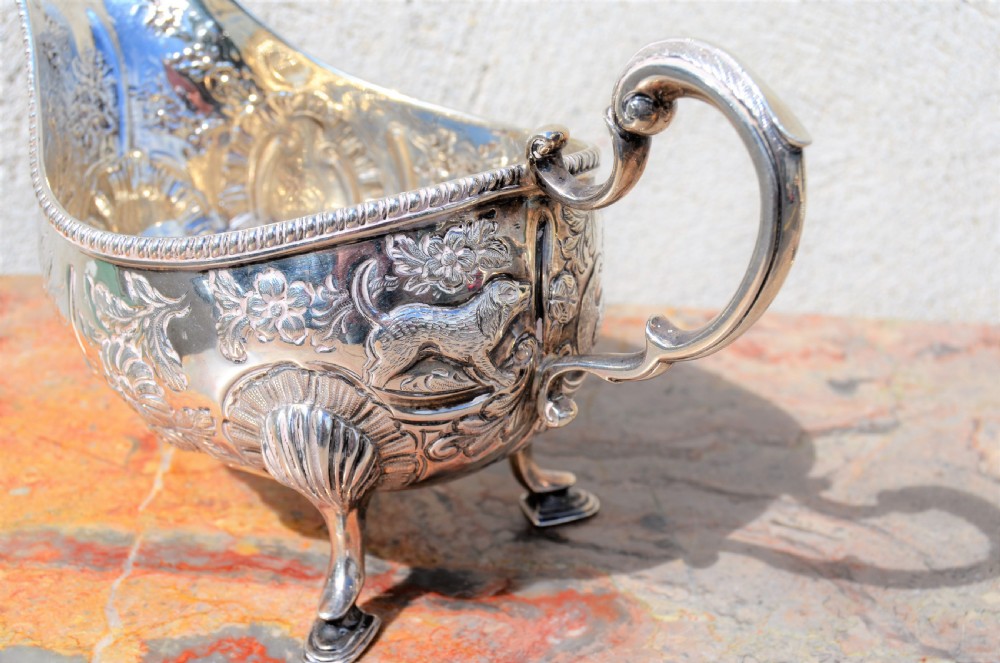 A matching pair of silver sauce boats featuring ornate floral repousse chasing, double-scroll handles, and shell-capped pad feet. View V