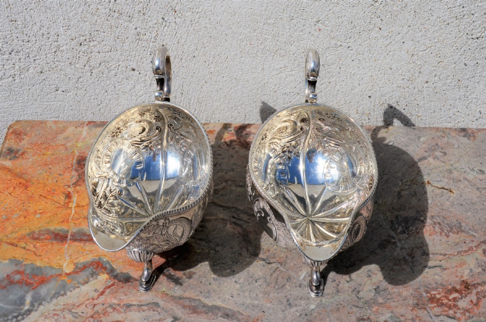 A matching pair of silver sauce boats featuring ornate floral repousse chasing, double-scroll handles, and shell-capped pad feet. View VI